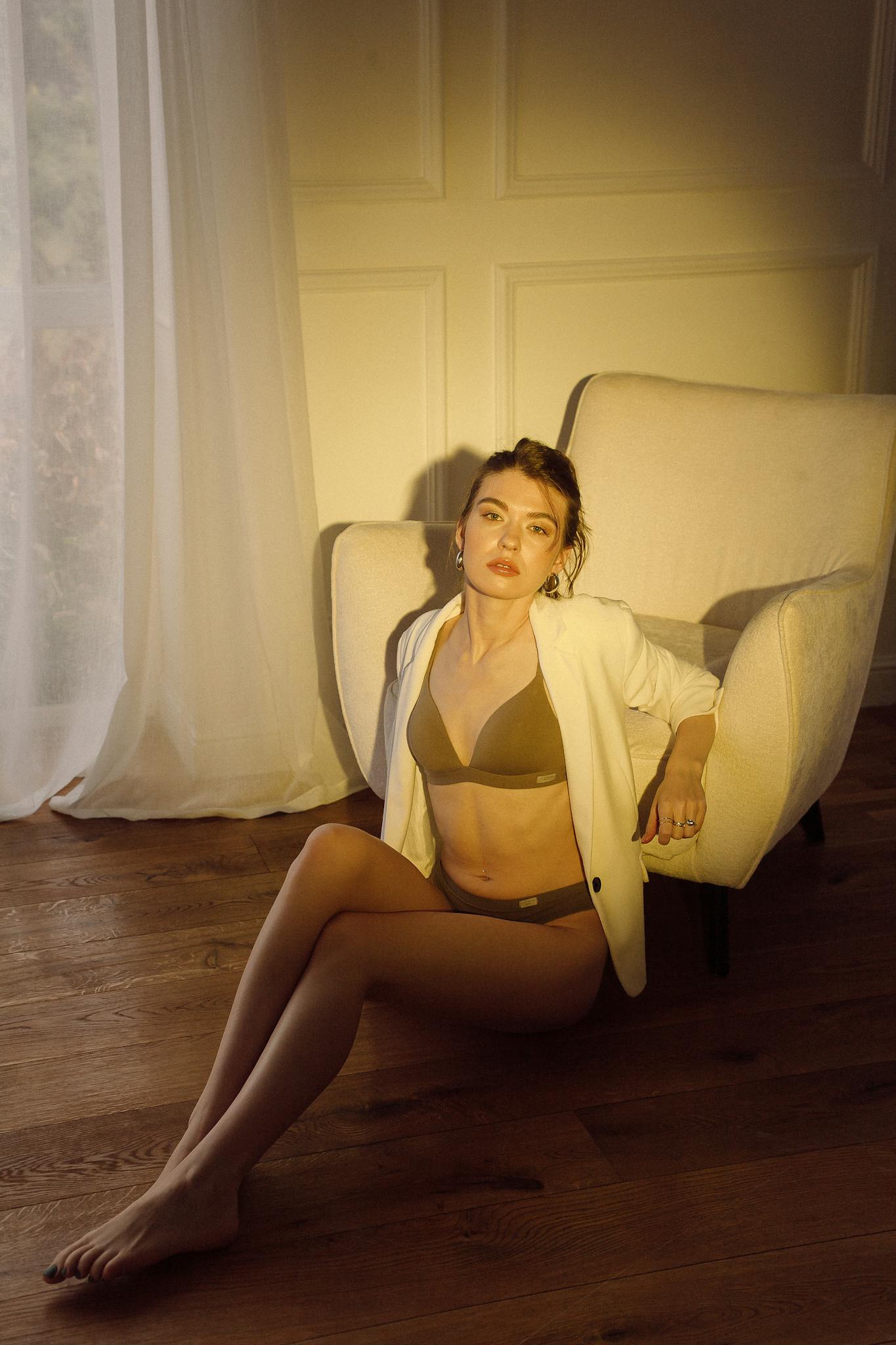 A stylish woman poses in elegant lingerie with sunlight streaming through a window, casting warm tones.