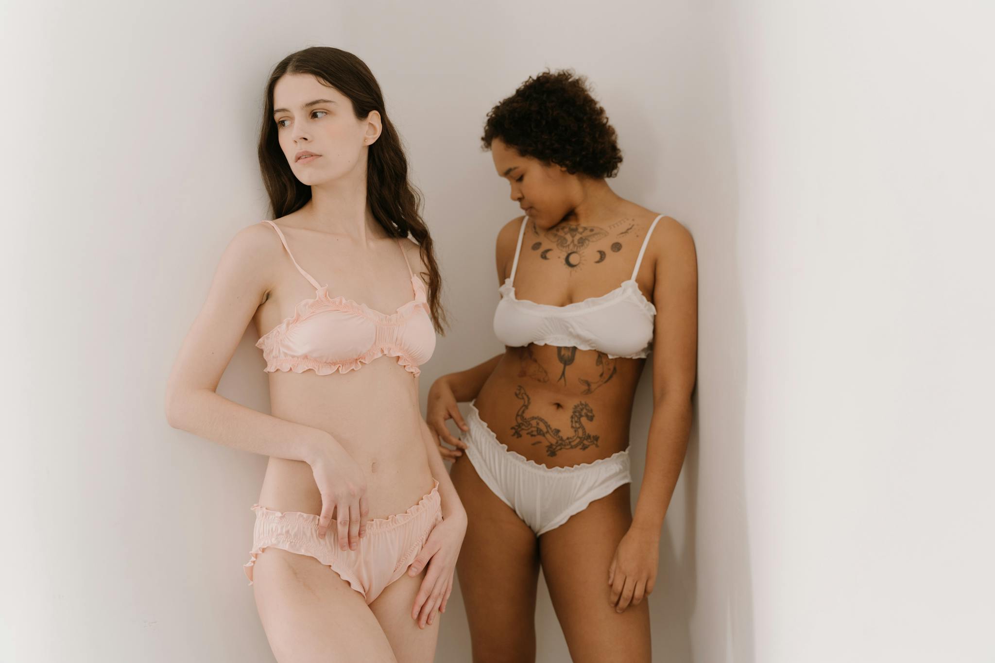 Elegant and artistic portrait of two women in lingerie showcasing body tattoos and femininity.